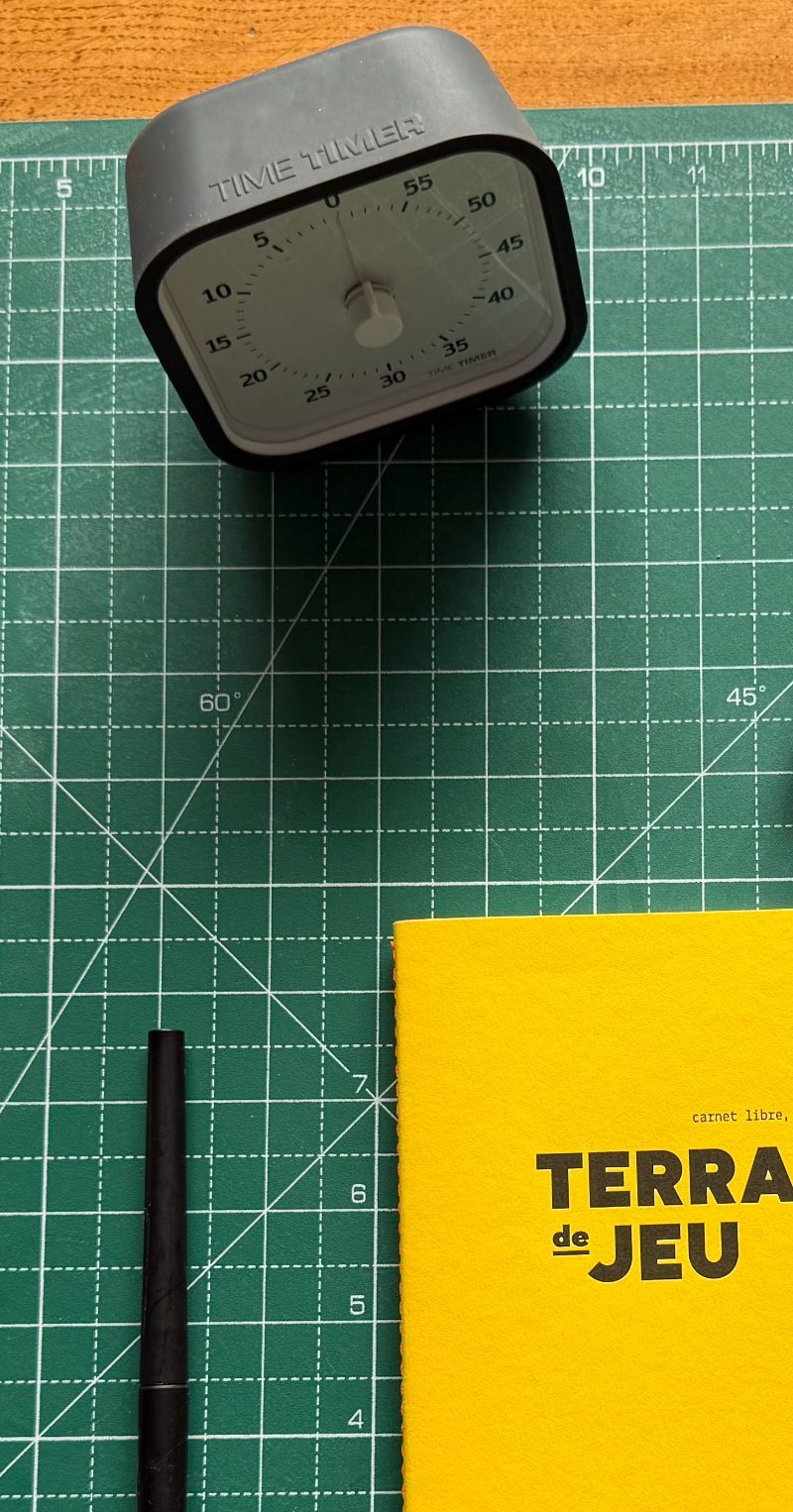 Minuteur, stylo et carnet Terrain de jeu posés sur un tapis de découpe, prêts pour un entretien